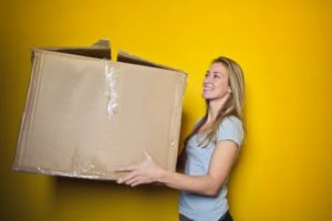 woman holding a large moving box against a yellow wall