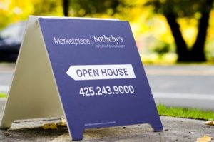 An open house sale sign on a sidewalk with trees in the background