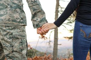 military man and wife holding hands in the woods