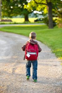 boy walking on dirt path with backpack on