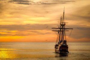 old wooden ship sailing on the water at sunset